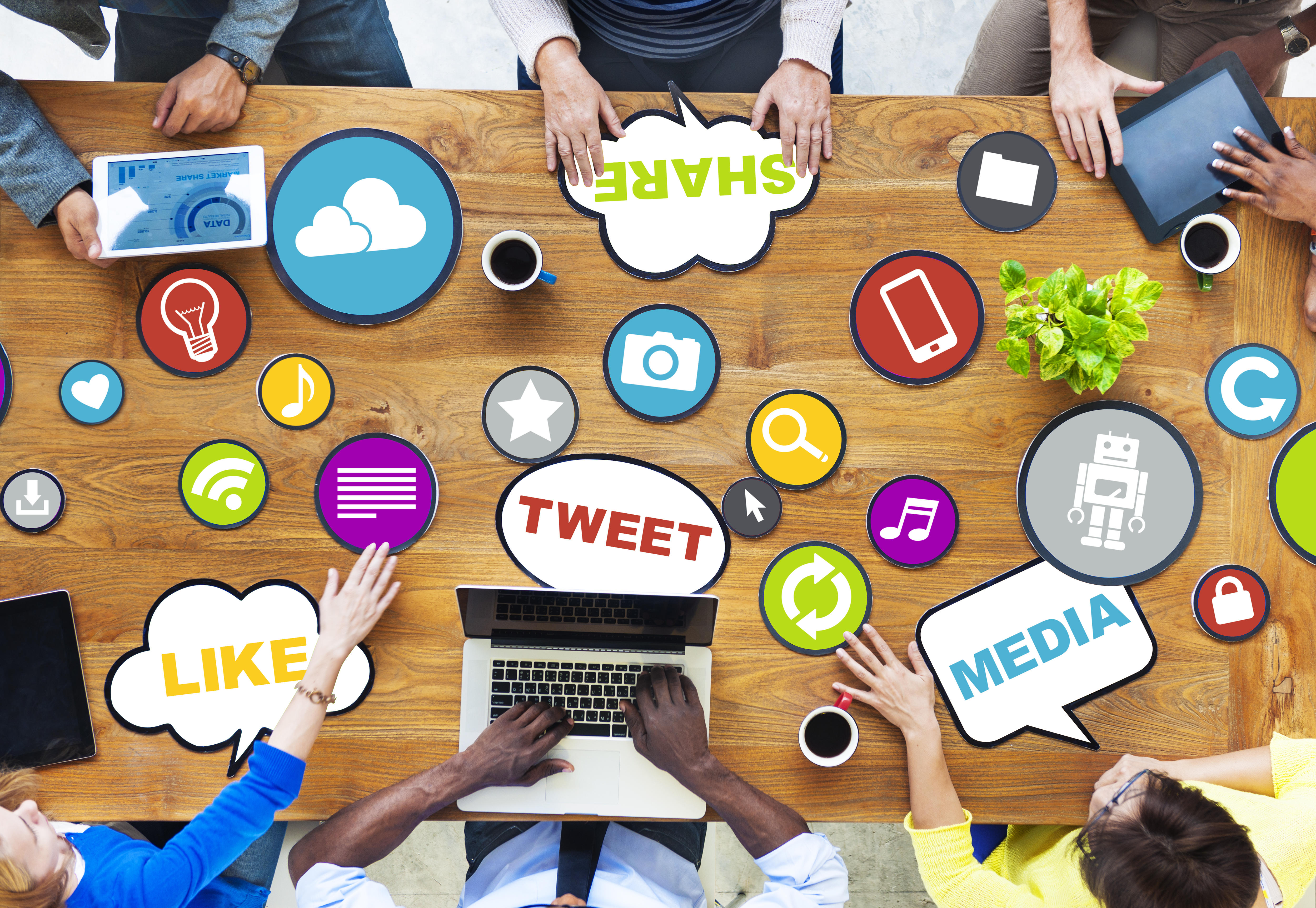 Overhead view of a table with six busniess people and icons spread around related to social media, such as like, tweet, and share